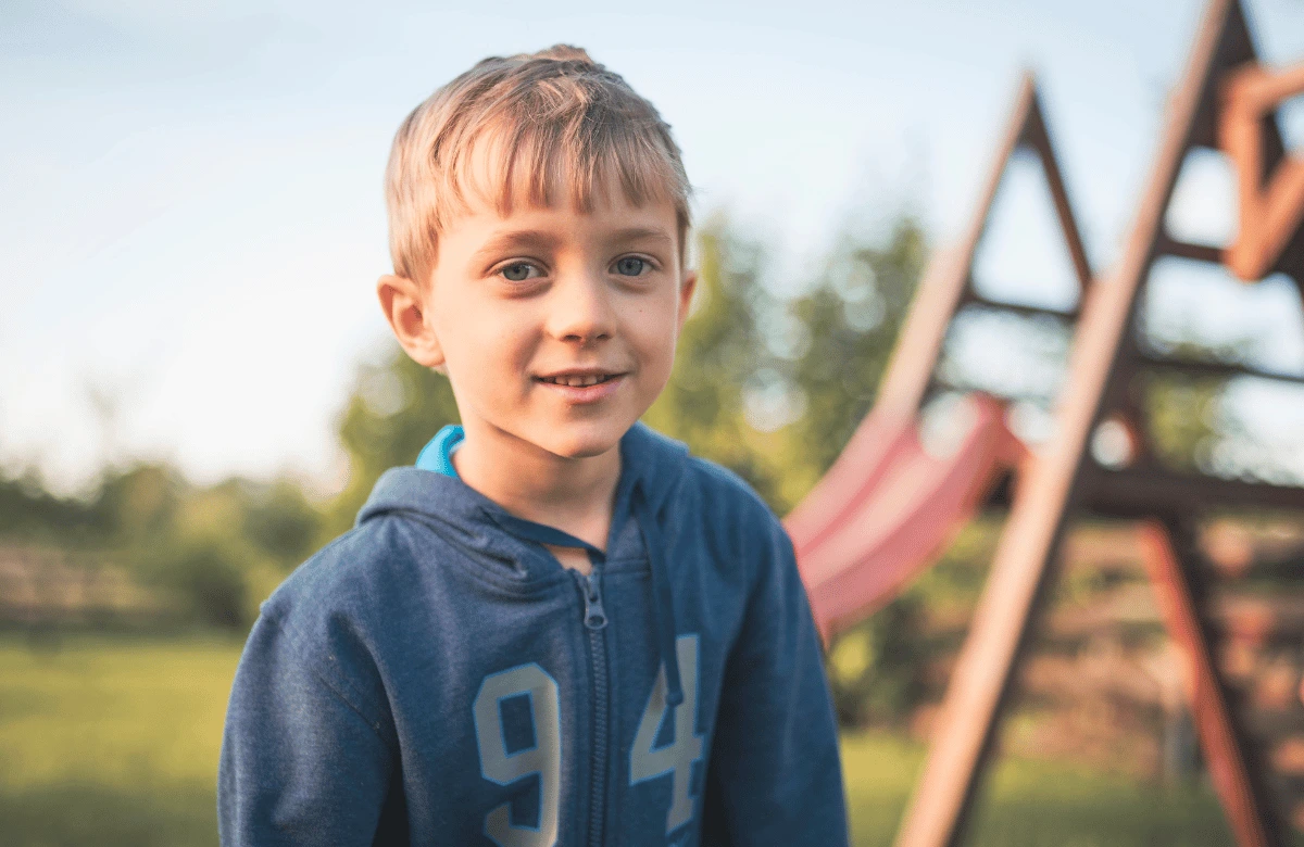 a young boy standing outside by a playground