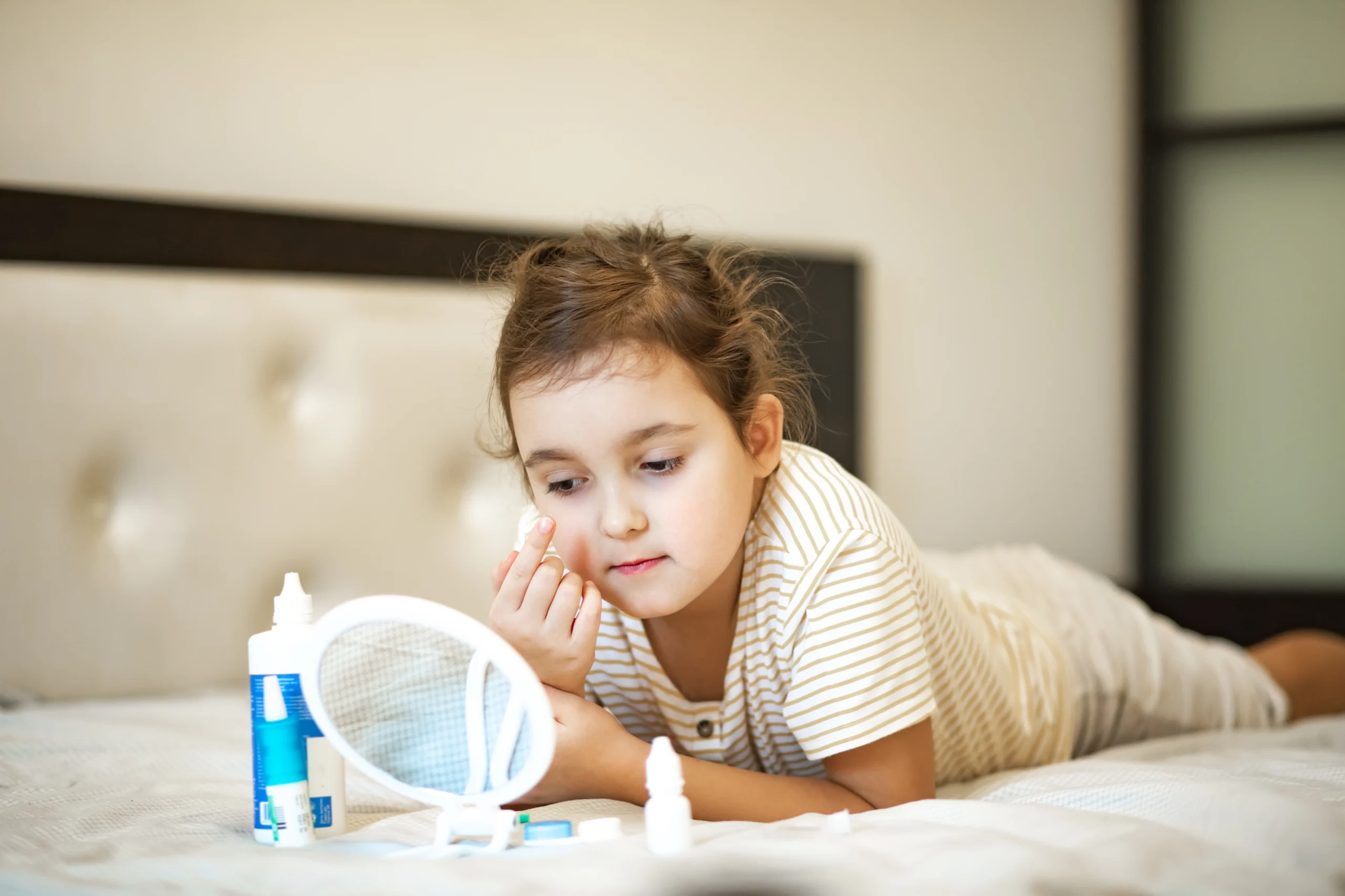 A young girl puts on contact lenses with the help of a small mirror.