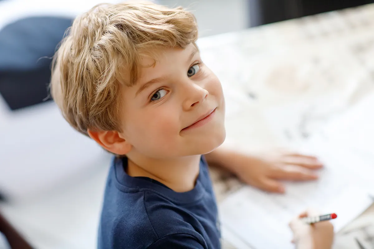 a young boy smiling and doing homework