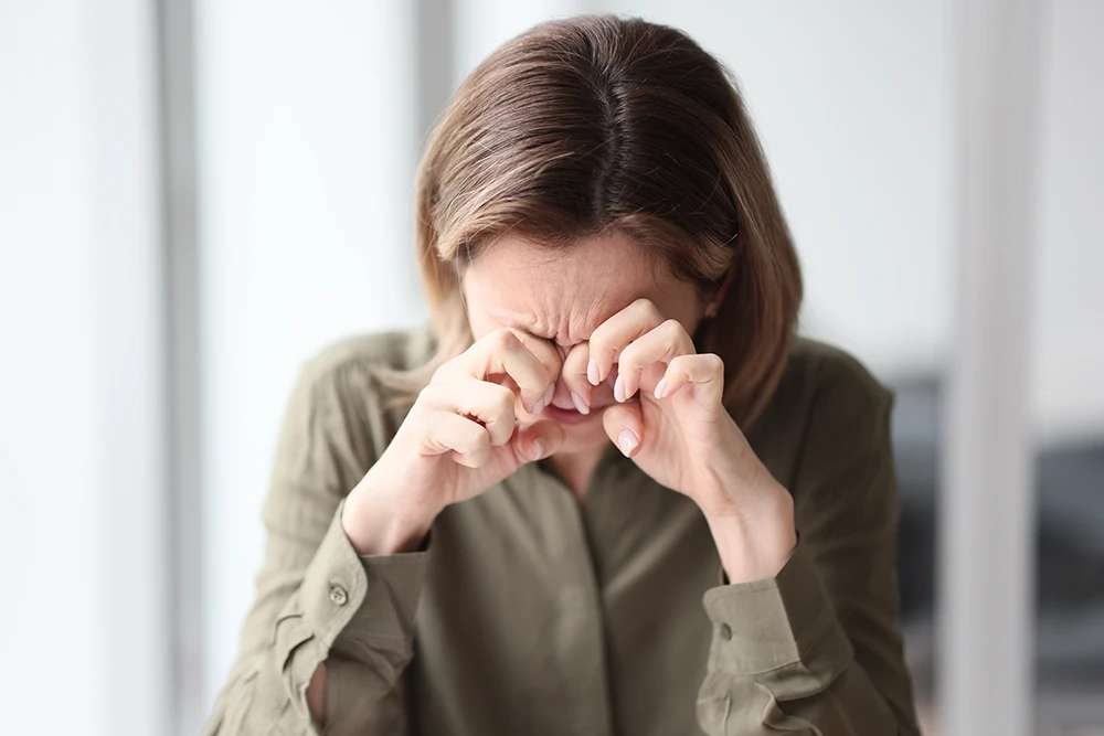 adult-vision-therapy a woman sitting at a table holding her hands to her eyes in pain